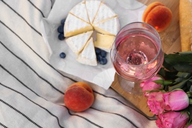 Photo of Glass of delicious rose wine, flowers and food on white picnic blanket