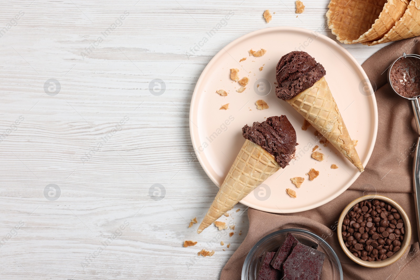 Photo of Chocolate ice cream scoops in wafer cones and candies on light wooden table, flat lay. Space for text