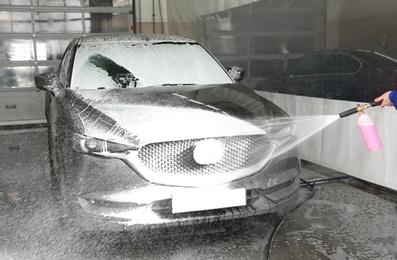 Worker cleaning automobile with high pressure water jet at car wash