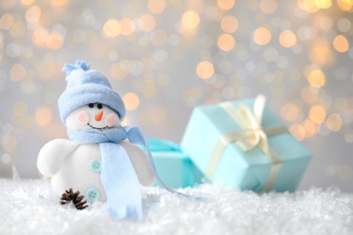 Photo of Snowman toy on snow against blurred festive lights, space for text. Christmas decoration