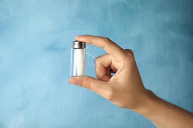 Photo of Woman holding glass jar with biodegradable dental floss against light blue background, closeup