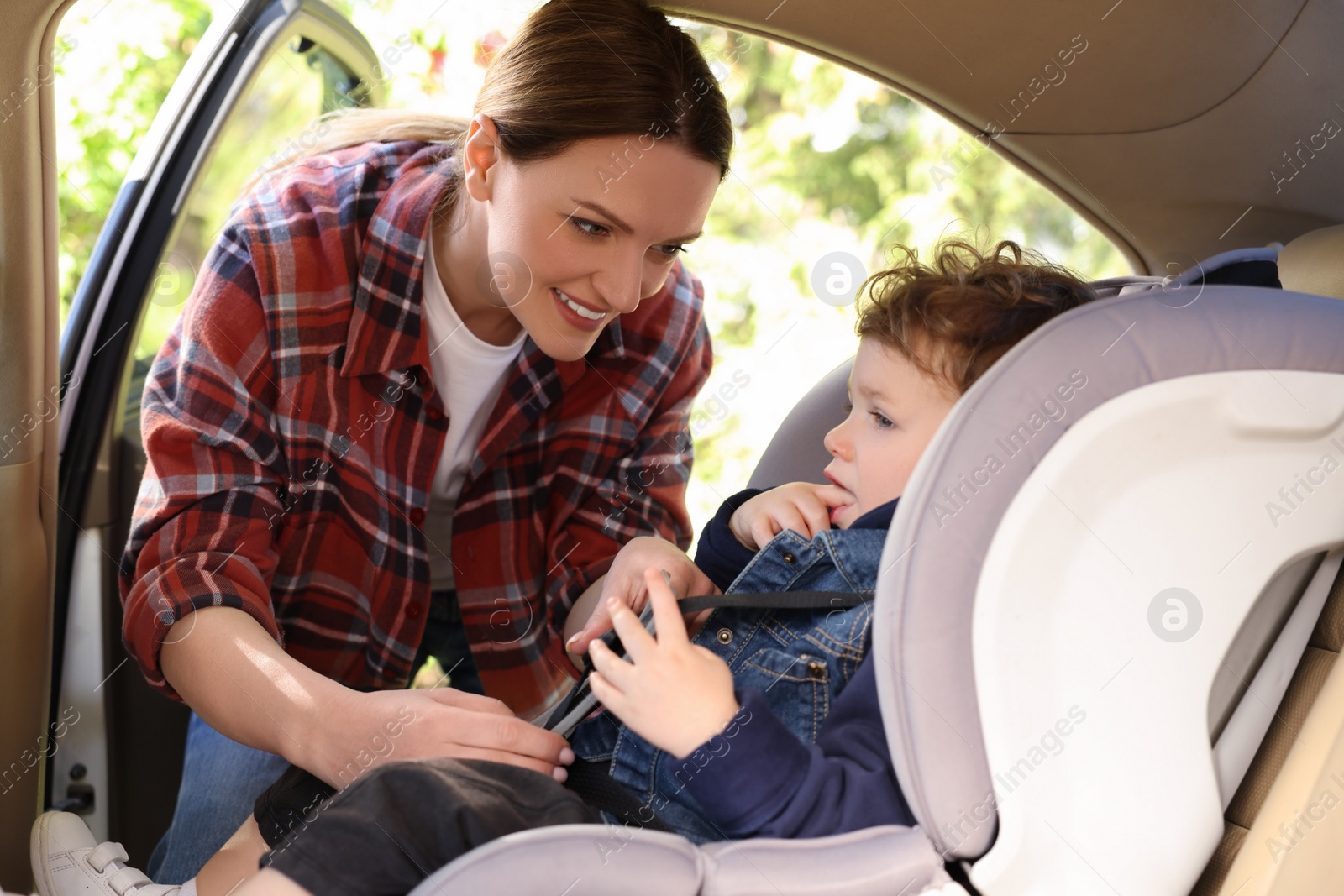 Photo of Mother fastening her son in child safety seat inside car