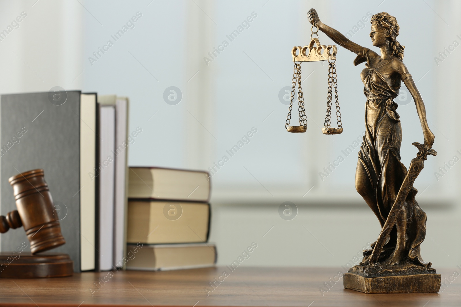 Photo of Figure of Lady Justice, gavel and books on wooden table indoors. Symbol of fair treatment under law