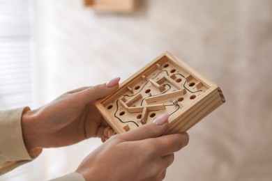 Photo of Woman holding wooden toy maze with metal ball on blurred background, closeup