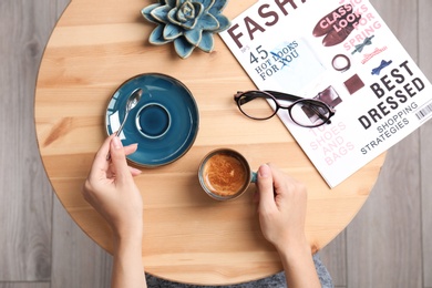 Photo of Young woman with cup of delicious hot coffee at table, top view