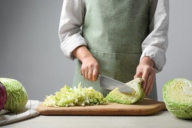 Photo of Woman cutting fresh savoy cabbage on board at wooden table, closeup