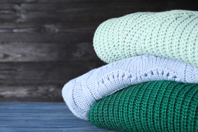 Image of Stack of folded warm sweaters on blue wooden table. Space for text