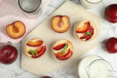 Delicious cupcakes with plums on white marble table, flat lay