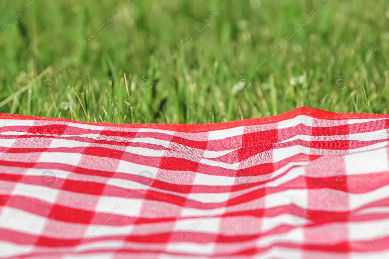 Photo of Checkered picnic tablecloth on fresh green grass, closeup