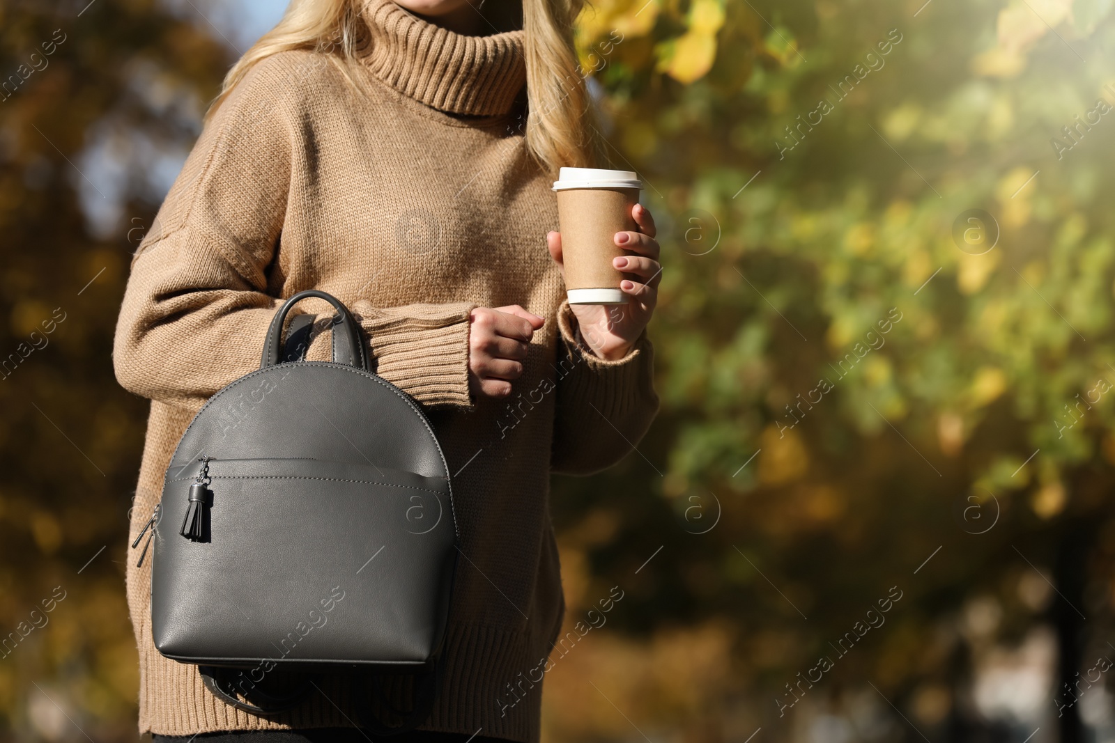 Photo of Young woman with stylish backpack and hot drink on autumn day, closeup. Space for text