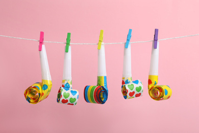 Photo of Party horns with pegs on laundry line against pink background. April Fool's Day
