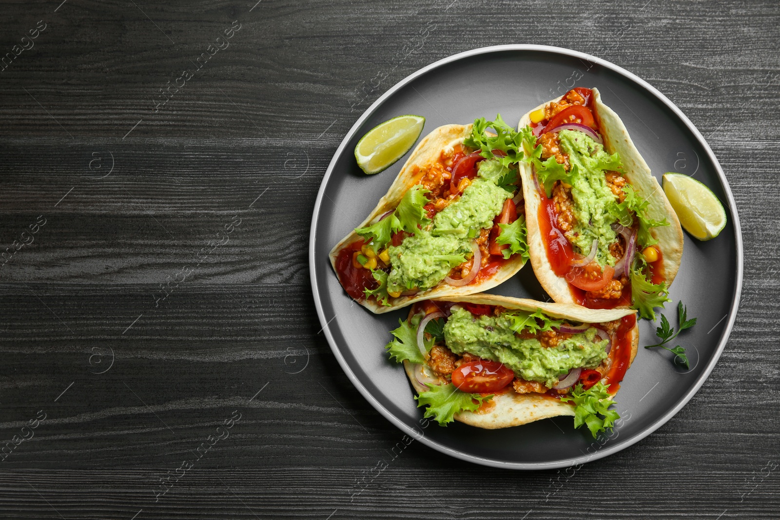 Photo of Delicious tacos with guacamole, meat and vegetables on wooden table, top view. Space for text