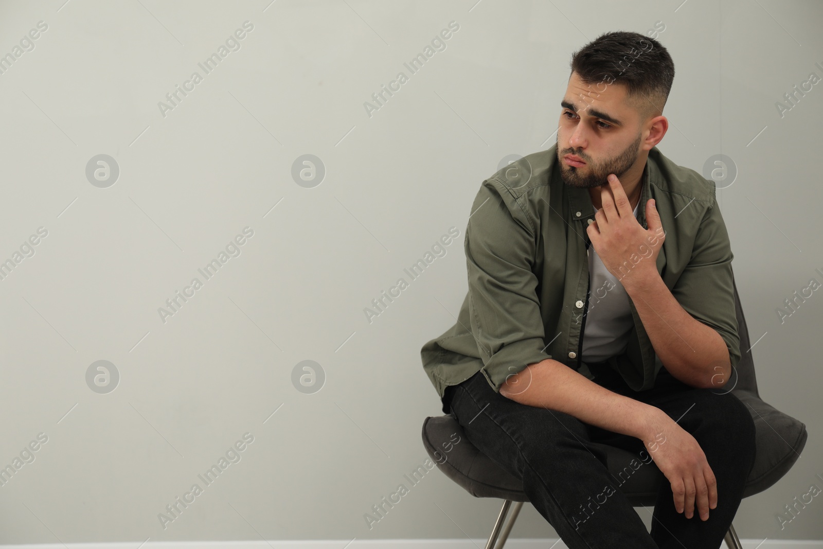 Photo of Sad man sitting near light grey wall. Space for text