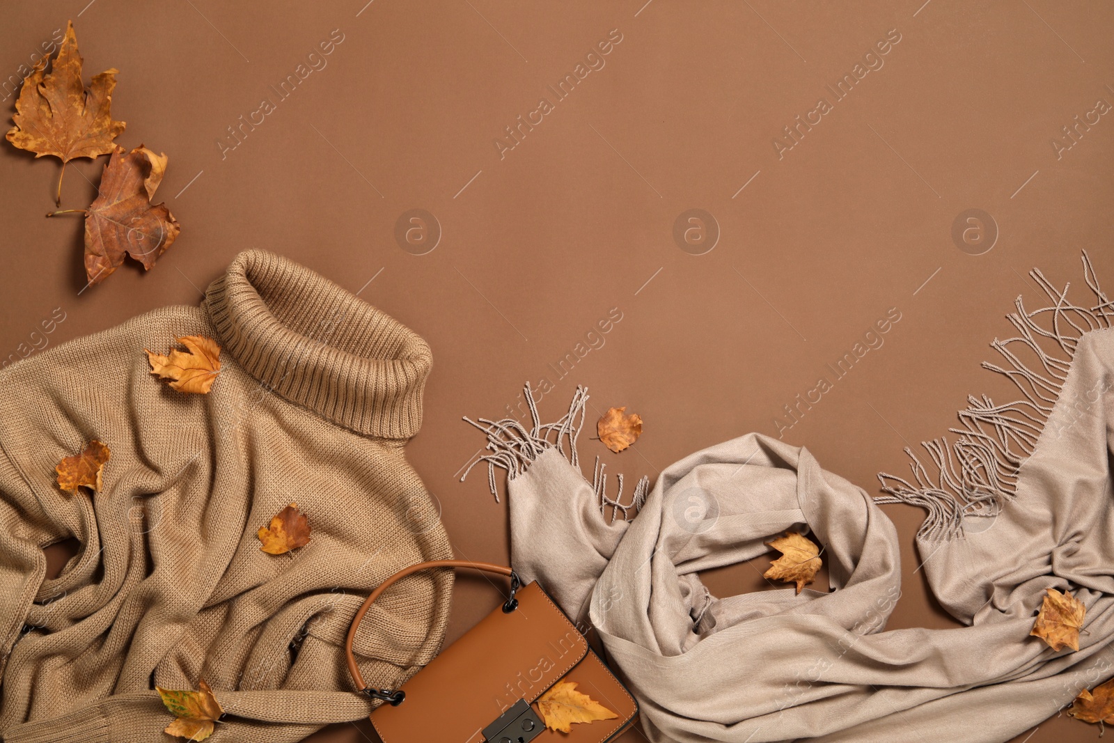 Photo of Flat lay composition with sweater and dry leaves on brown background, space for text. Autumn season