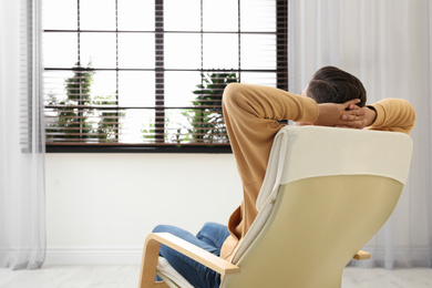 Photo of Man relaxing in armchair near window at home, back view