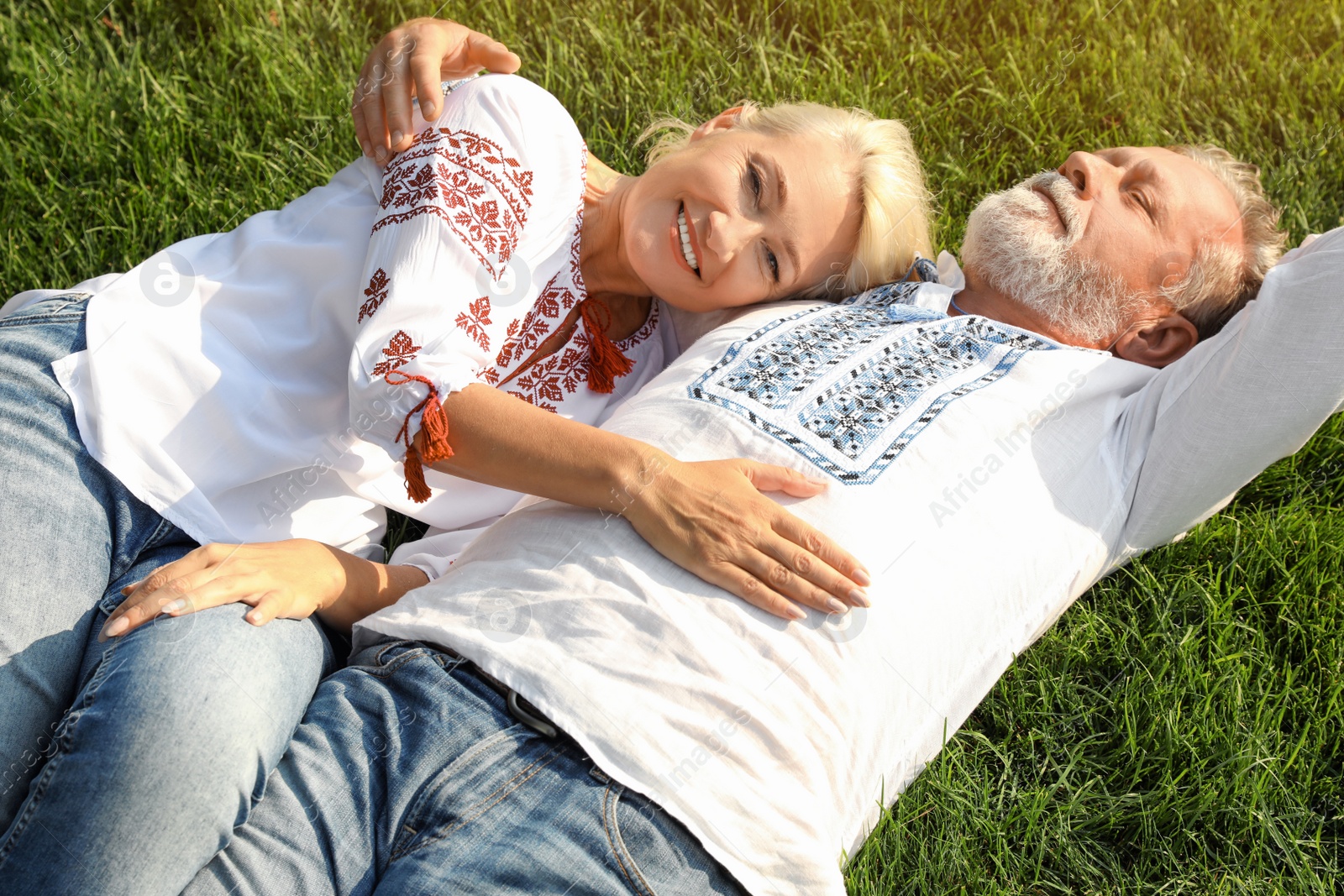 Photo of Happy mature couple in Ukrainian national clothes resting on green grass outdoors