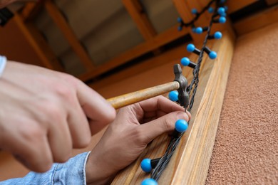 Man decorating house with Christmas lights outdoors, closeup