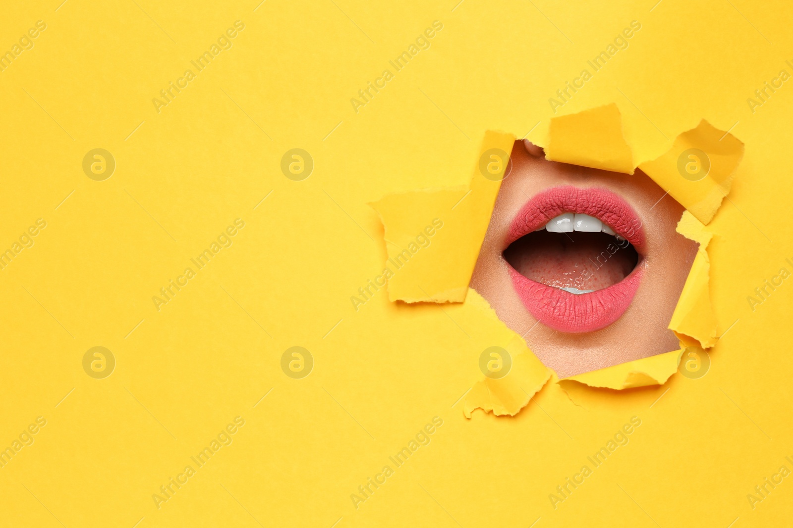 Photo of Lips of young woman with beautiful lipstick visible through hole in color paper. Space for text