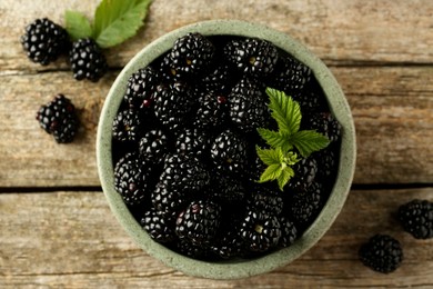 Photo of Bowl and fresh ripe blackberries on wooden table, flat lay