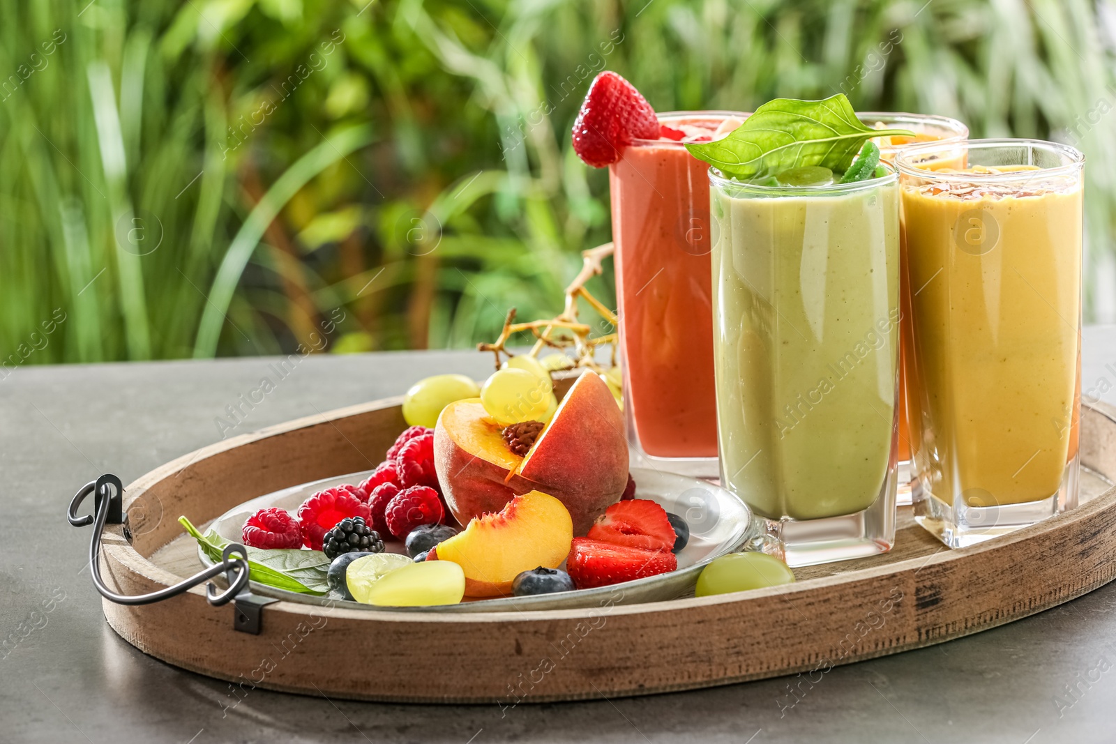 Photo of Tray with different delicious smoothies and ingredients on grey table against blurred background