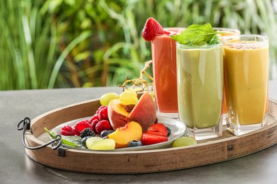 Photo of Tray with different delicious smoothies and ingredients on grey table against blurred background