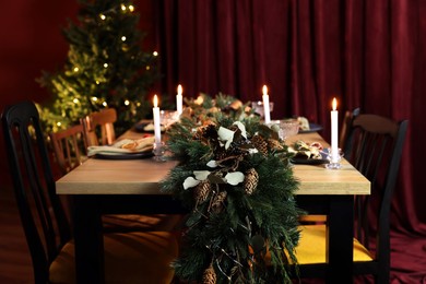 Dining table with burning candles and Christmas decor in stylish room. Interior design