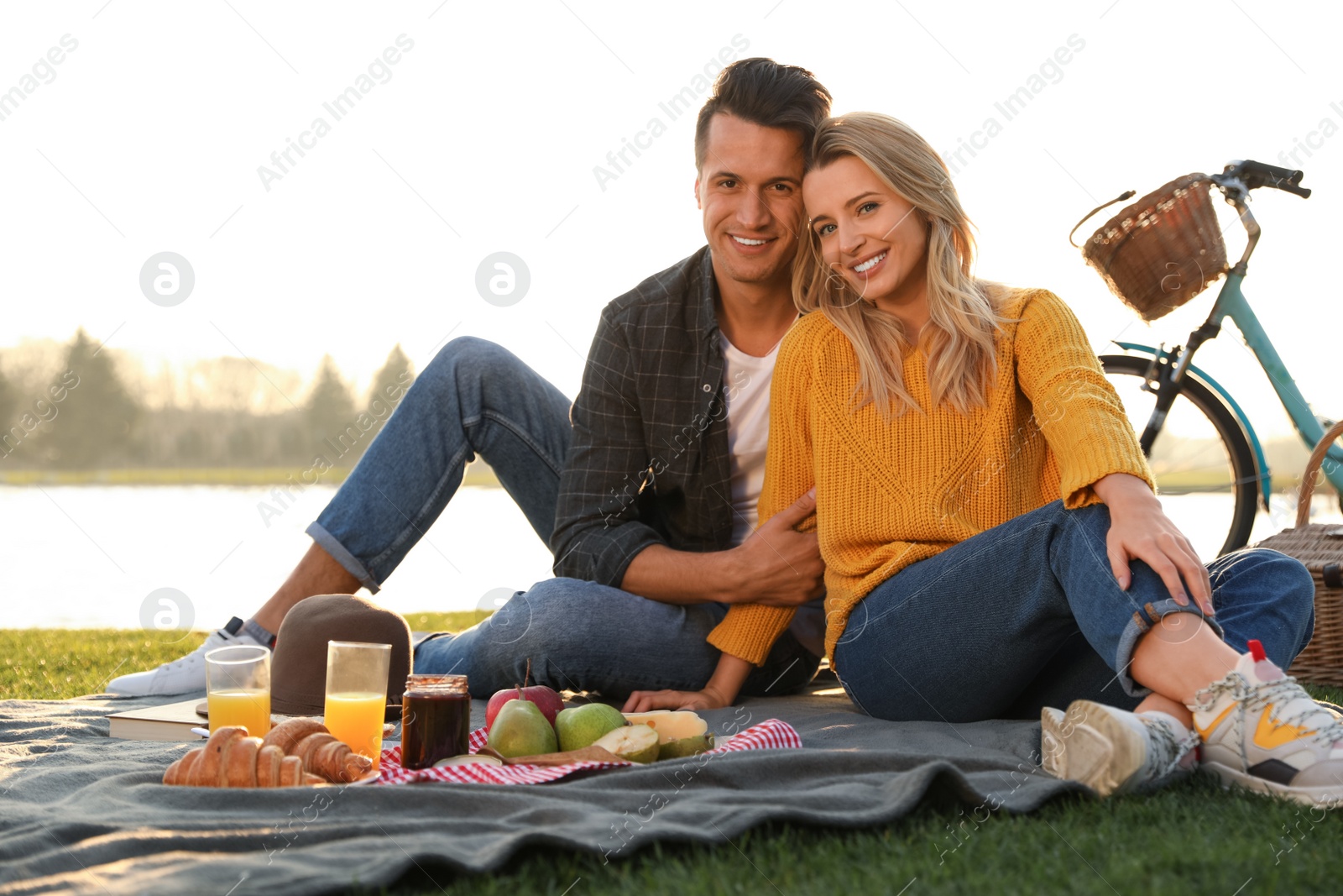 Photo of Happy young couple having picnic near lake on sunny day