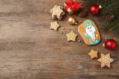 Photo of Tasty gingerbread cookies and festive decor on wooden table, flat lay with space for text. St. Nicholas Day celebration