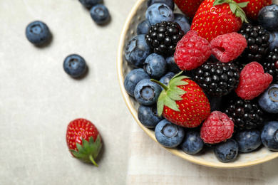 Photo of Mix of different fresh berries in bowl on light grey table, flat lay. Space for text