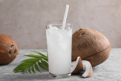 Photo of Glass of coconut water with ice cubes, palm leaf and nuts on grey table