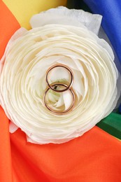 Wedding rings and flower on rainbow LGBT flag, top view