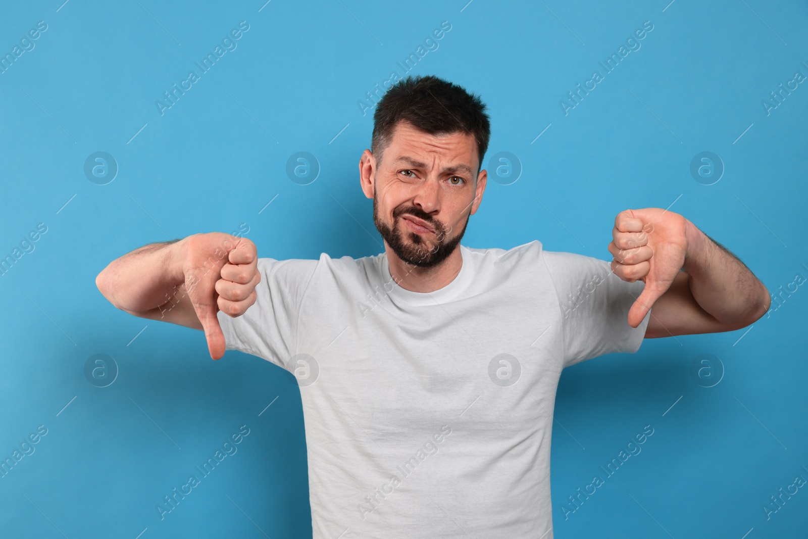 Photo of Man showing thumbs down on light blue background