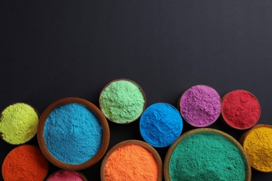 Photo of Colorful powders in bowls on black background, flat lay with space for text. Holi festival celebration