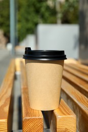 Takeaway cardboard coffee cup with plastic lid on wooden bench outdoors