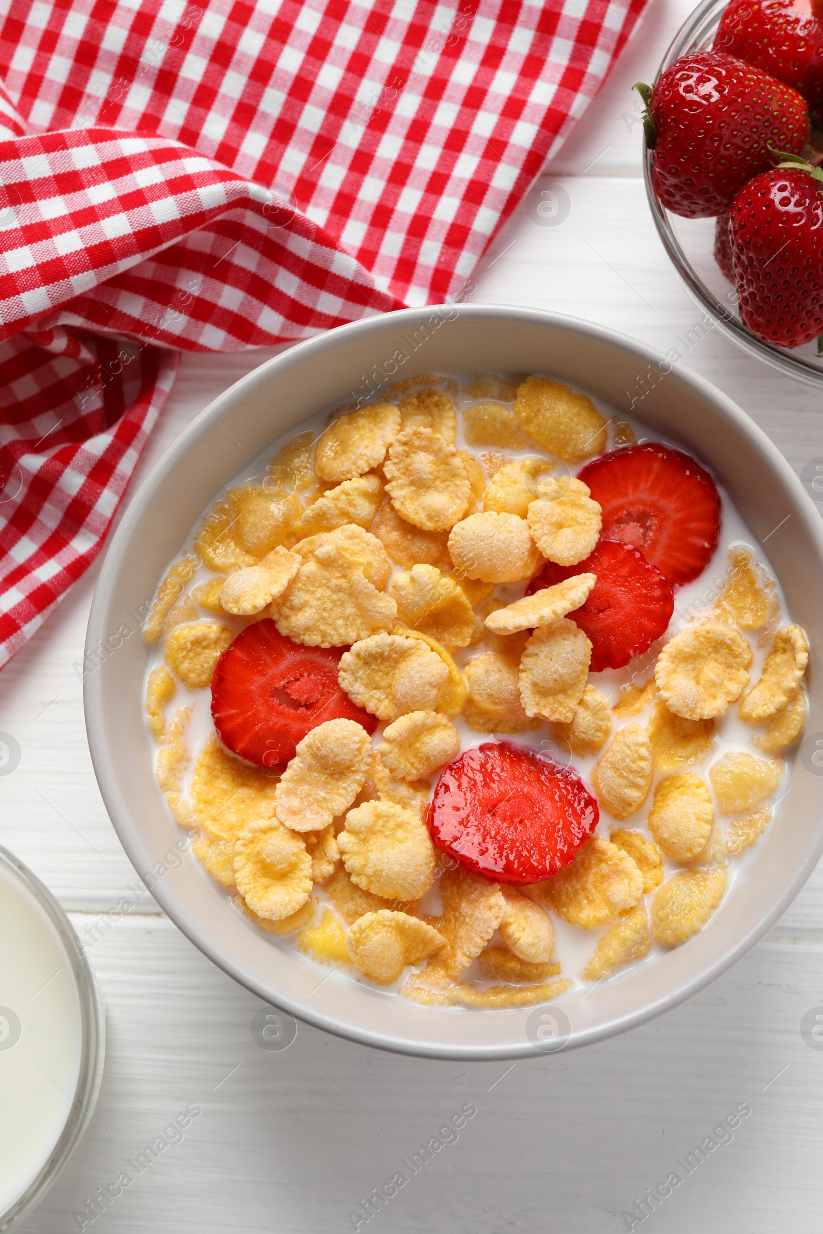 Photo of Corn flakes with strawberries in bowl served on white wooden table, flat lay