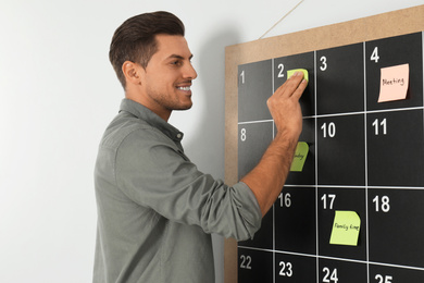 Handsome man putting sticky note on board calendar