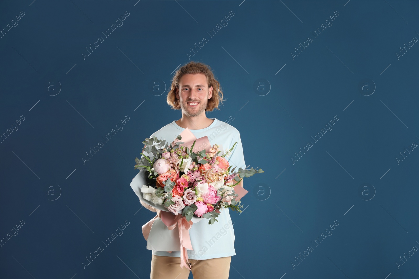 Photo of Young handsome man with beautiful flower bouquet on blue background