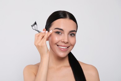 Beautiful young woman with eyelash curler on white background