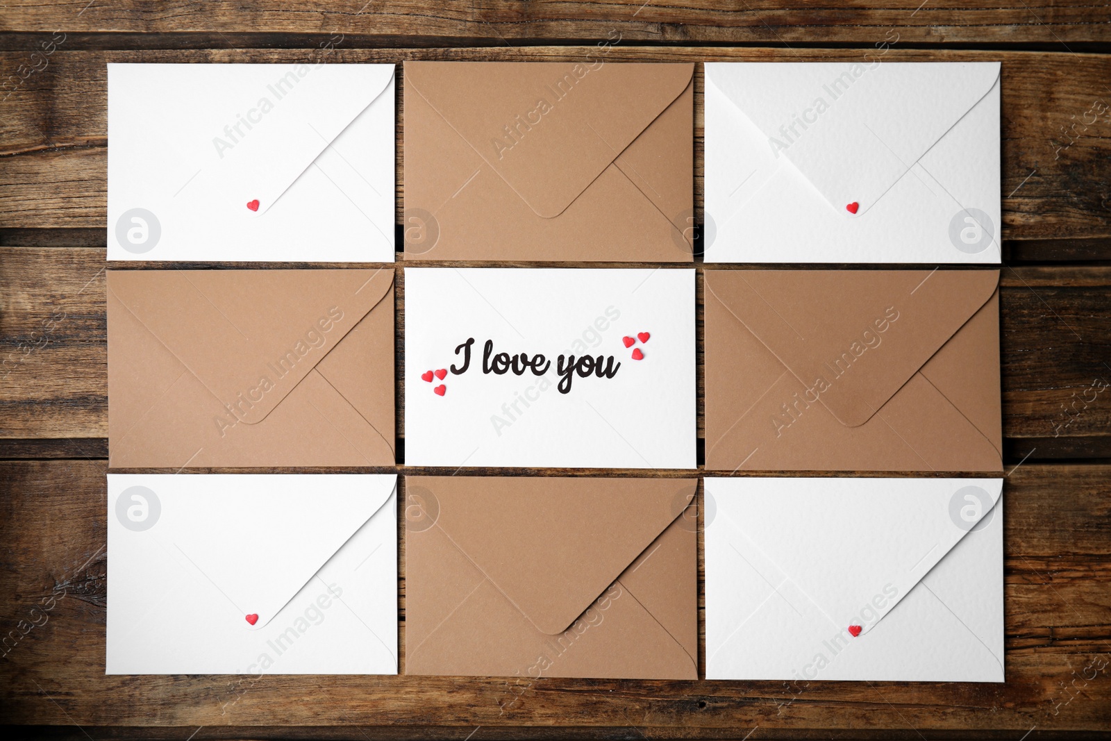 Photo of Sheet of paper with phrase I Love You, envelopes and heart shaped sprinkles on wooden table, flat lay