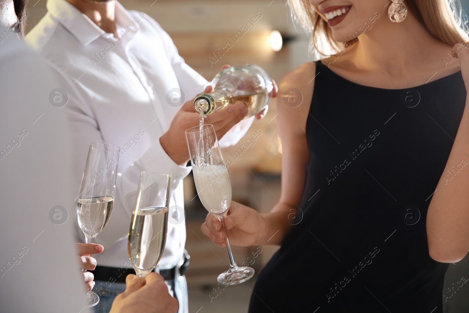 Photo of Man pouring champagne into glasses at party indoors, closeup