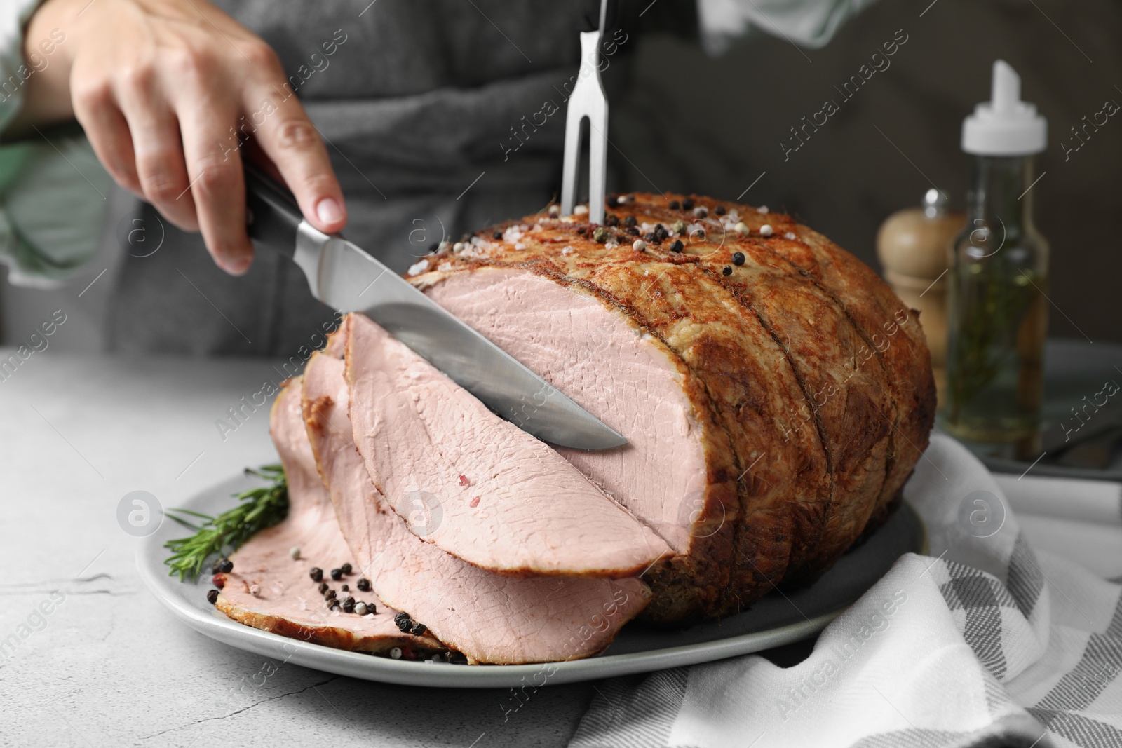 Photo of Woman cutting delicious baked ham at light grey table, closeup