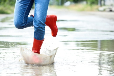 Photo of Woman with red rubber boots running in puddle, closeup. Rainy weather
