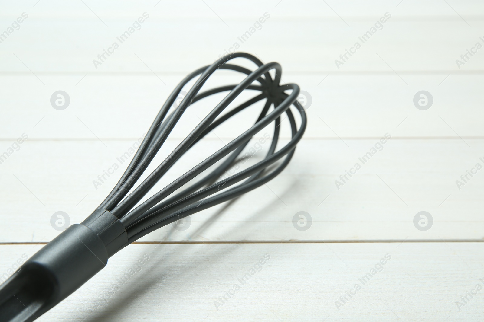 Photo of Plastic whisk on white wooden table, closeup. Space for text