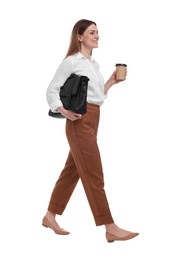 Beautiful businesswoman with briefcase and paper cup of coffee walking on white background
