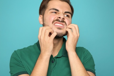 Young man scratching face on color background. Annoying itch