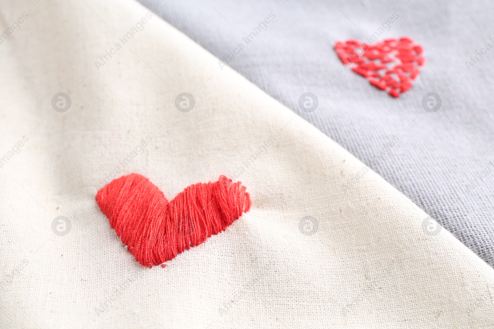 Photo of Embroidered red hearts on light and gray cloth, closeup