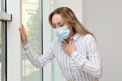 Photo of Young woman in medical mask suffering from pain during breathing near window