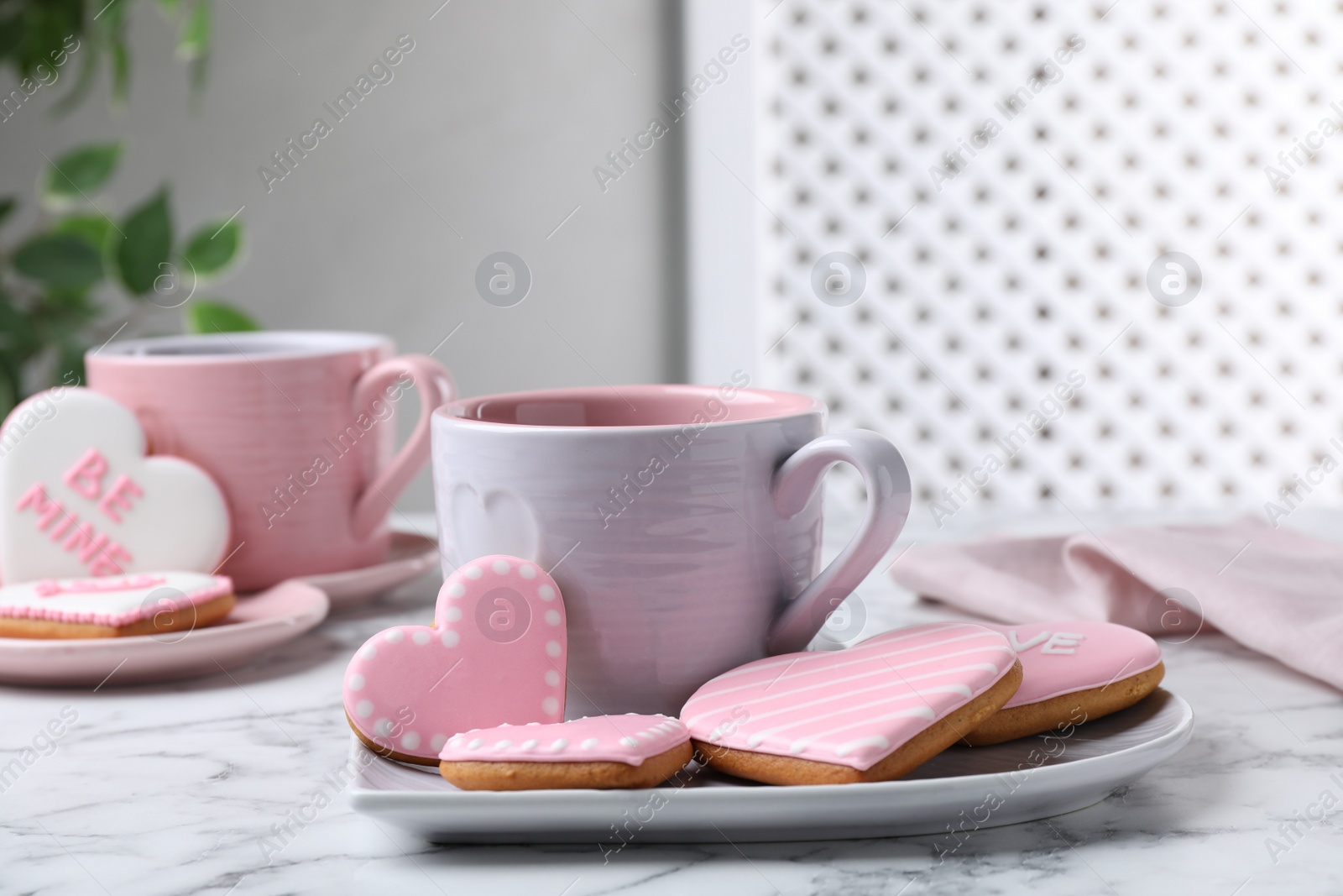 Photo of Delicious heart shaped cookies and cup of hot drink on white marble table
