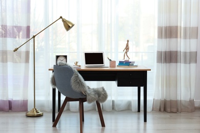 Stylish workplace interior with laptop on table near window. Space for text