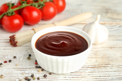 Photo of Composition with bowl of barbecue sauce on white wooden table